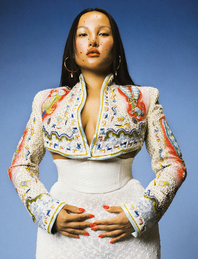 Tsunaina wears red and gold glass mushroom hoop earrings, embroidered matador jacket, white leather corset belt, and off-white knit skirt, all by Casablanca. - © System Magazine