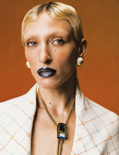 Maggie wears white and gold resin dome earrings, arch landscape chain bolo tie, and tennis check jumpsuit, all by Casablanca. - © System Magazine