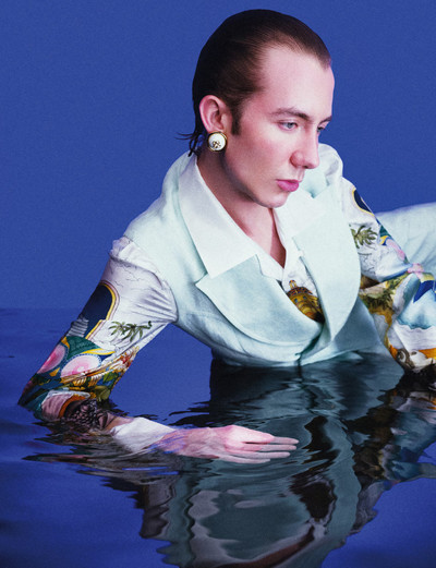 Paul wears mint linen sleeveless jacket, printed cuban collar silk shirt, and white and gold resin dome earrings, all by Casablanca. - © System Magazine