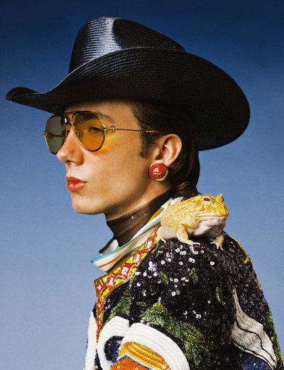 Paul wears midnight sail stetson cowboy straw hat, red and gold resin dome earrings, printed mesh top, printed cuban collar silk shirt, embroidered jacket, and yellow tinted 18k gold plated metal aviator frames, all by Casablanca. - © System Magazine