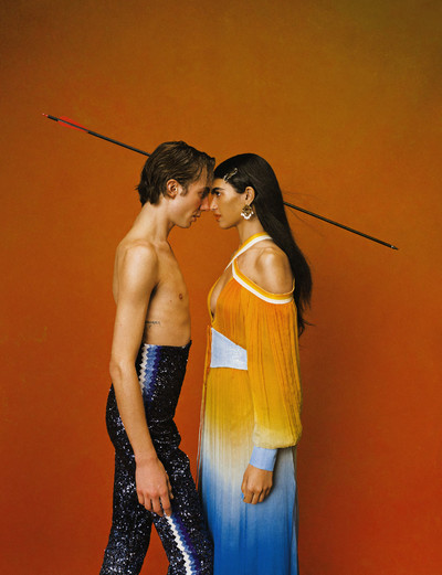 Paul wears navy embroidered matador trousers by Casablanca. Anita wears blue leather corset belt, Caza metal hair clip with crystals, monogram pearl drop earrings, and blue and orange gradient chiffon dress, all by Casablanca. - © System Magazine